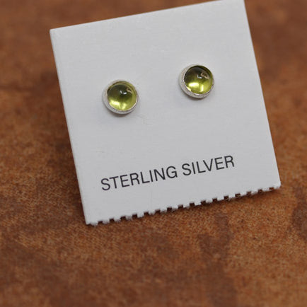 A pair of sterling silver peridot earrings displayed on a brown textured background.