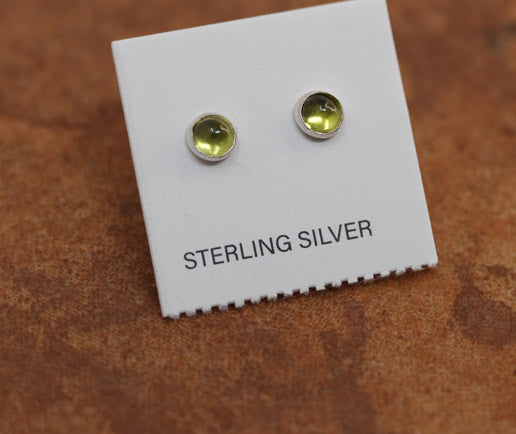 A pair of sterling silver peridot earrings displayed on a brown textured background.