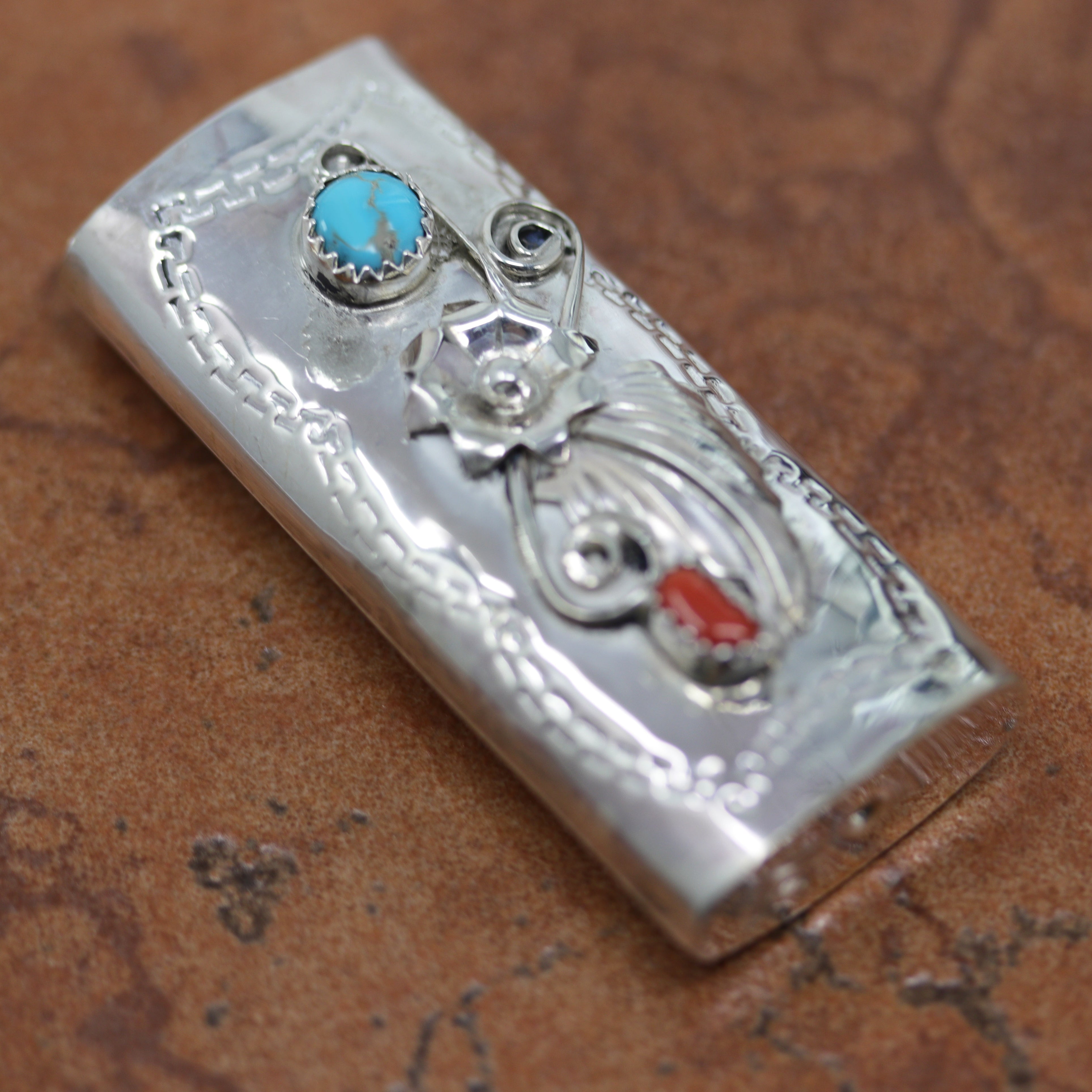 A lighter case made from sterling silver, turquoise, and coral. It measures 2 1/8" by 1".