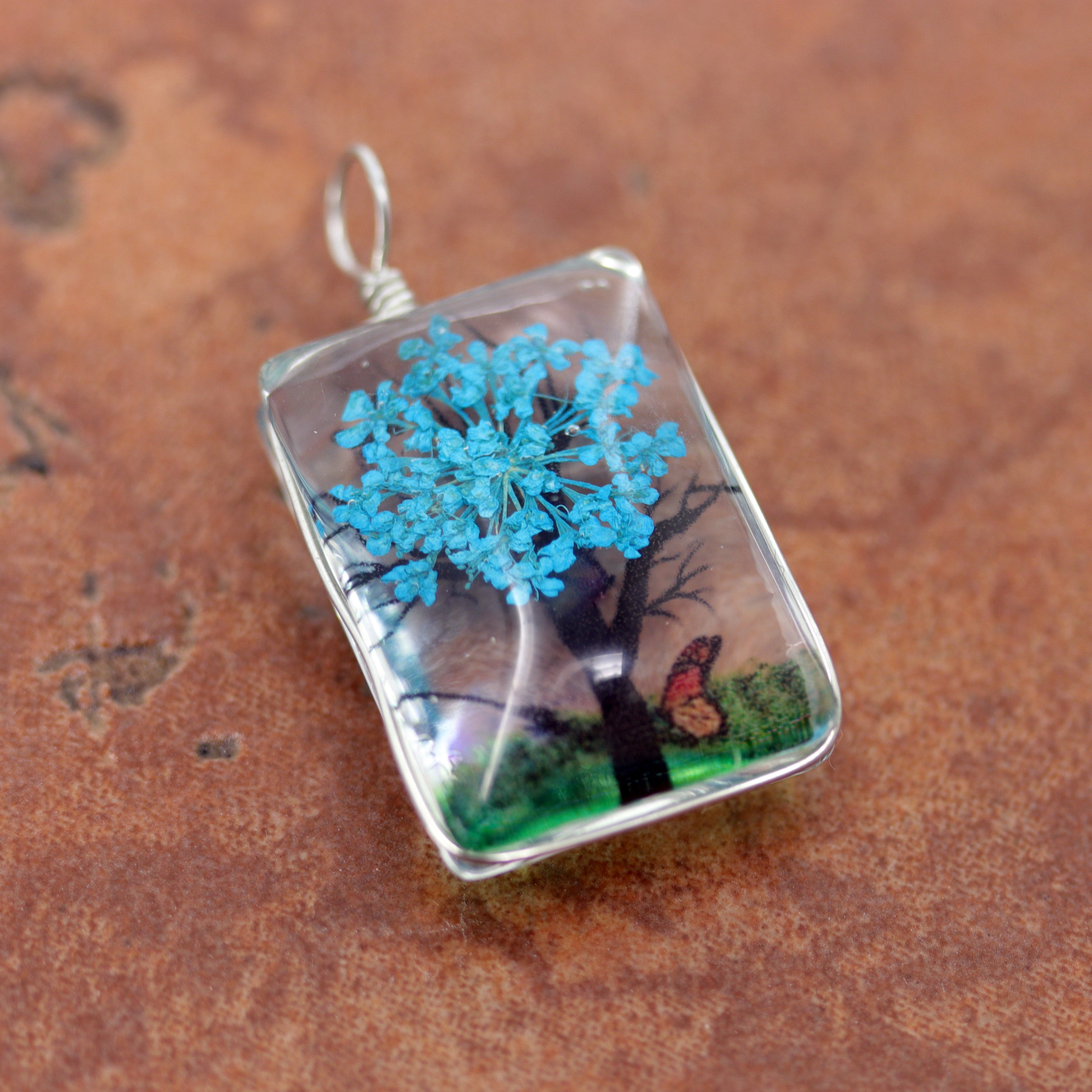 It is made from glass and purple flower petals. The pendant is about 1 3/8" in length including the bail, and about 3/4" wide.