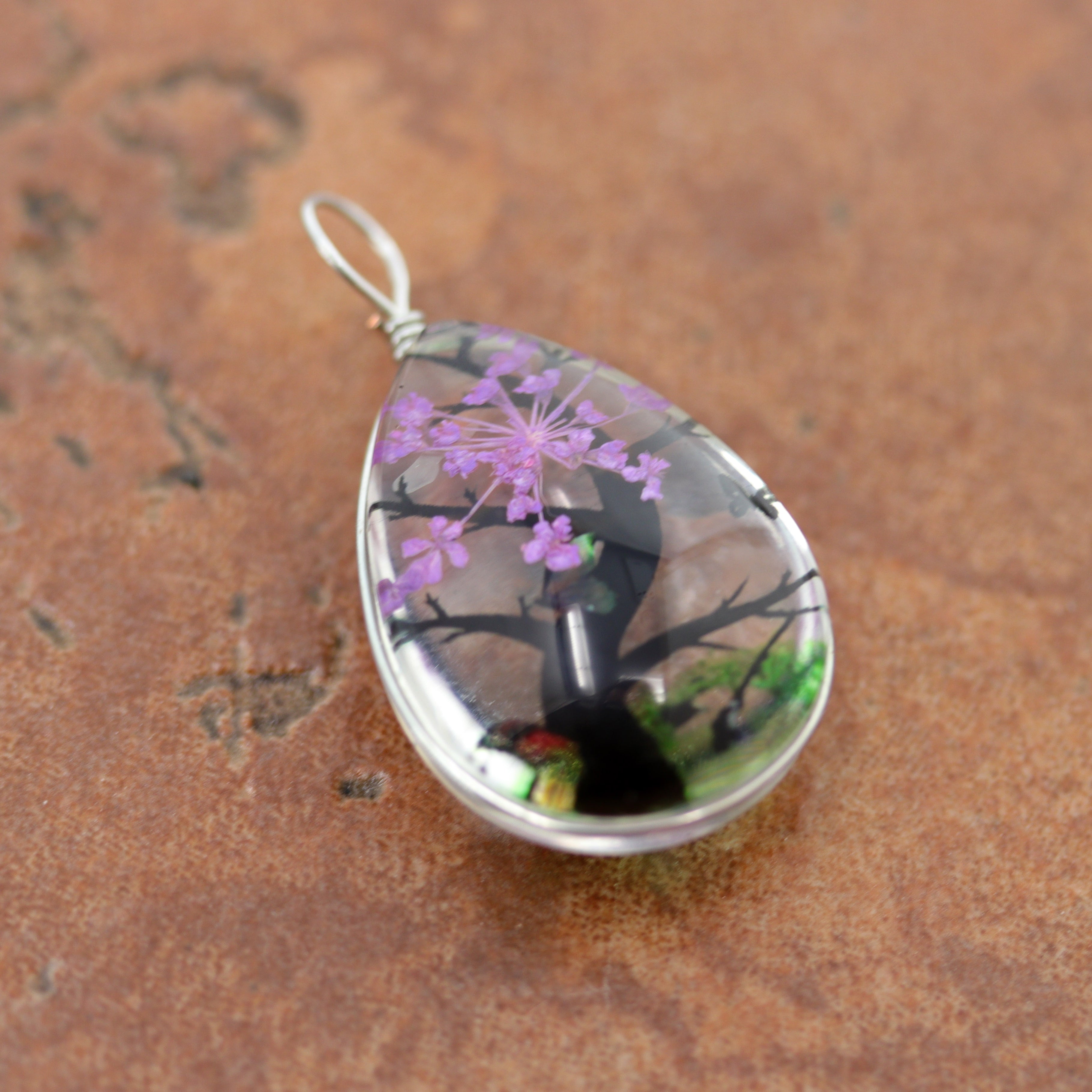 It is made from glass and purple flower petals. The pendant is about 1 3/8" in length including the bail, and about 3/4" wide.