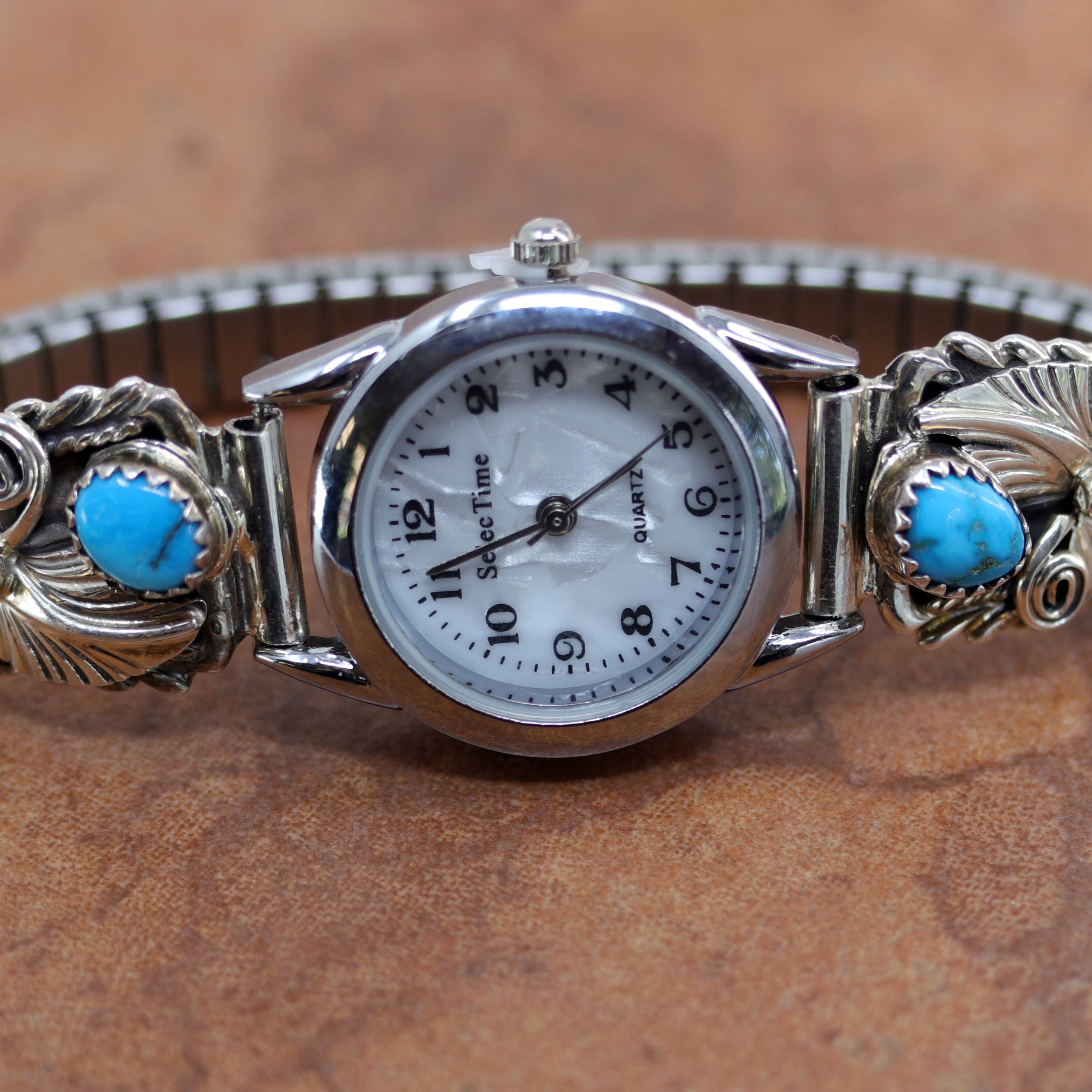 Silver watch with decorative band featuring turquoise and coral stones on a brown background