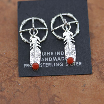 Circular earrings with a silver feather dropping down from them. There's is a small circular coral stone at the bottom of the feather