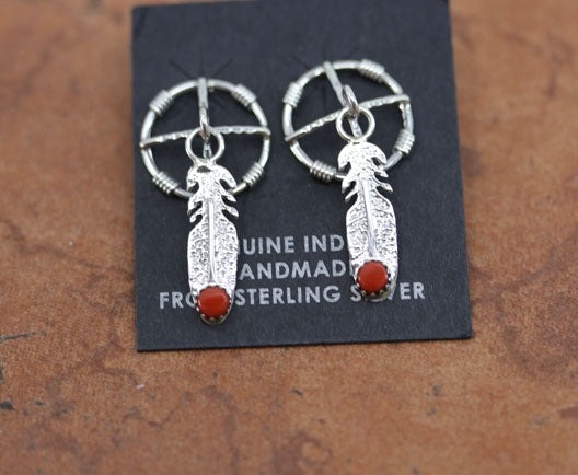 Circular earrings with a silver feather dropping down from them. There's is a small circular coral stone at the bottom of the feather